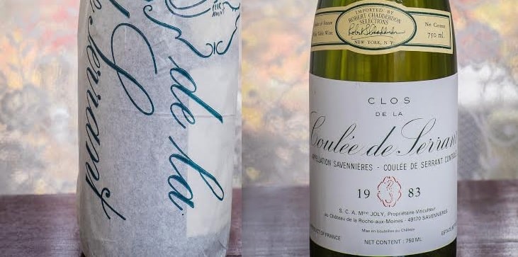 A vintage 1983 bottle of Clos de la Coulée de Serrant against a floral backdrop.