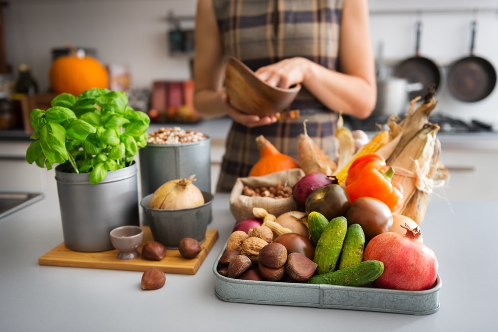 Assortment of Autumn fruits, nuts, and vegetables on a kitchen counter with basil and onion.