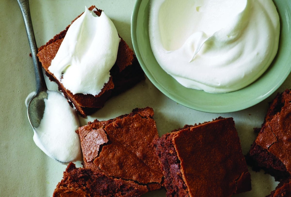 Dark chocolate bittersweet brownies with a glossy spoonful of cream on a vibrant background.