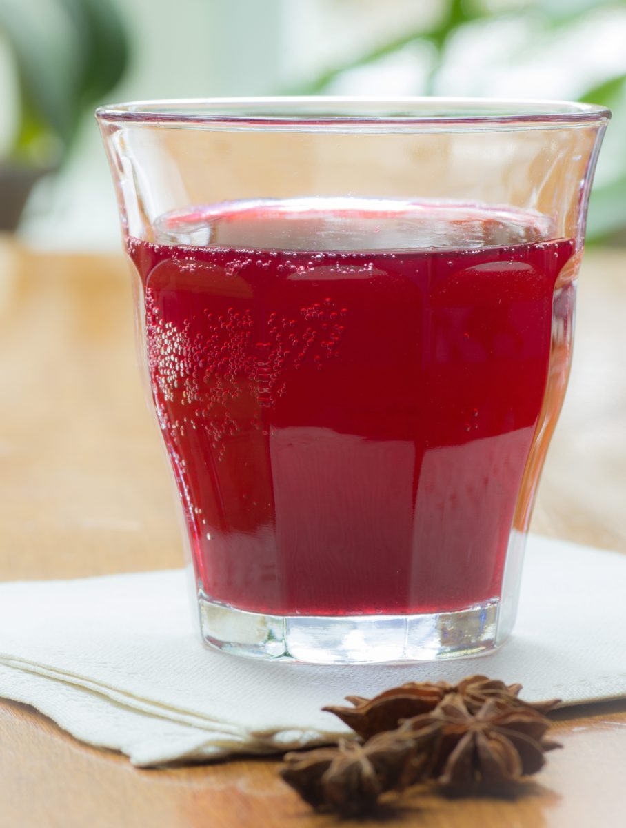 A vibrant red Black Currant Anise Shrub Mocktail with star anise beside it.