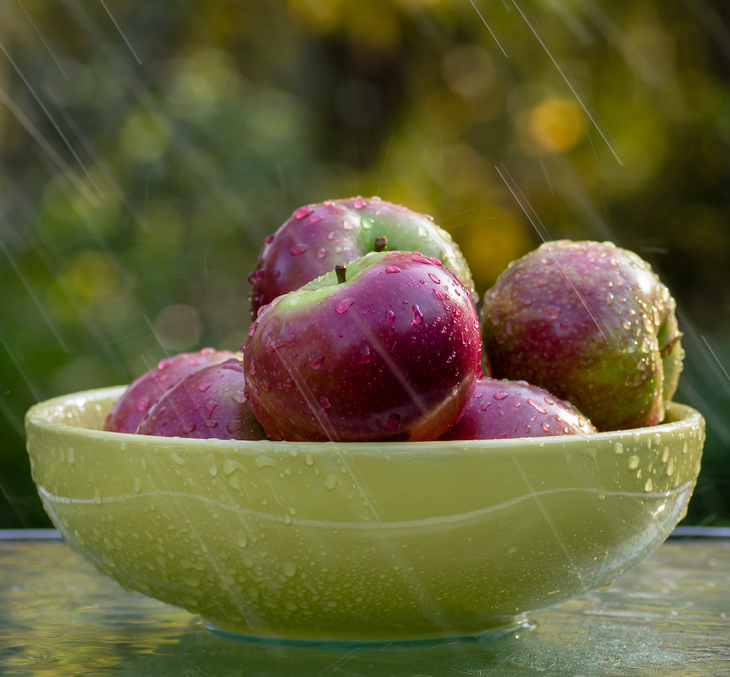 Fresh apples with raindrops in a green bowl.
