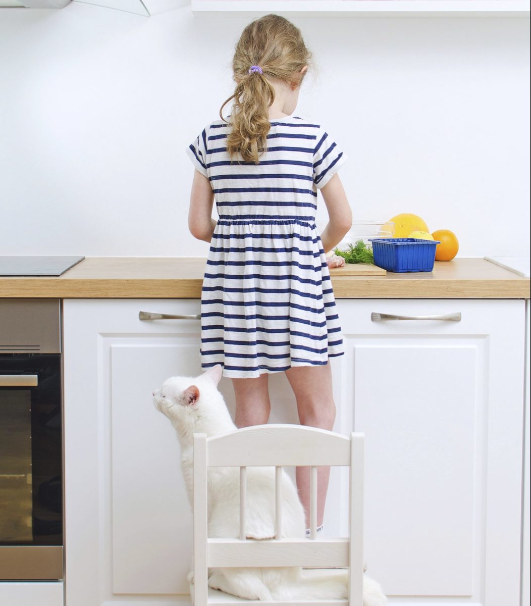 Back view of a little girl in a striped dress preparing food in the kitchen.