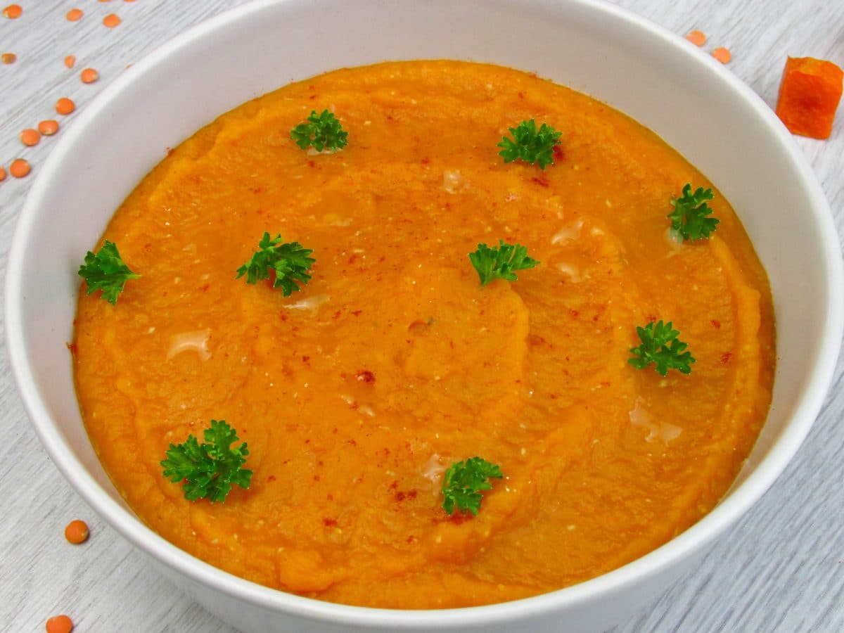Creamy orange carrot soup garnished with parsley in a white bowl