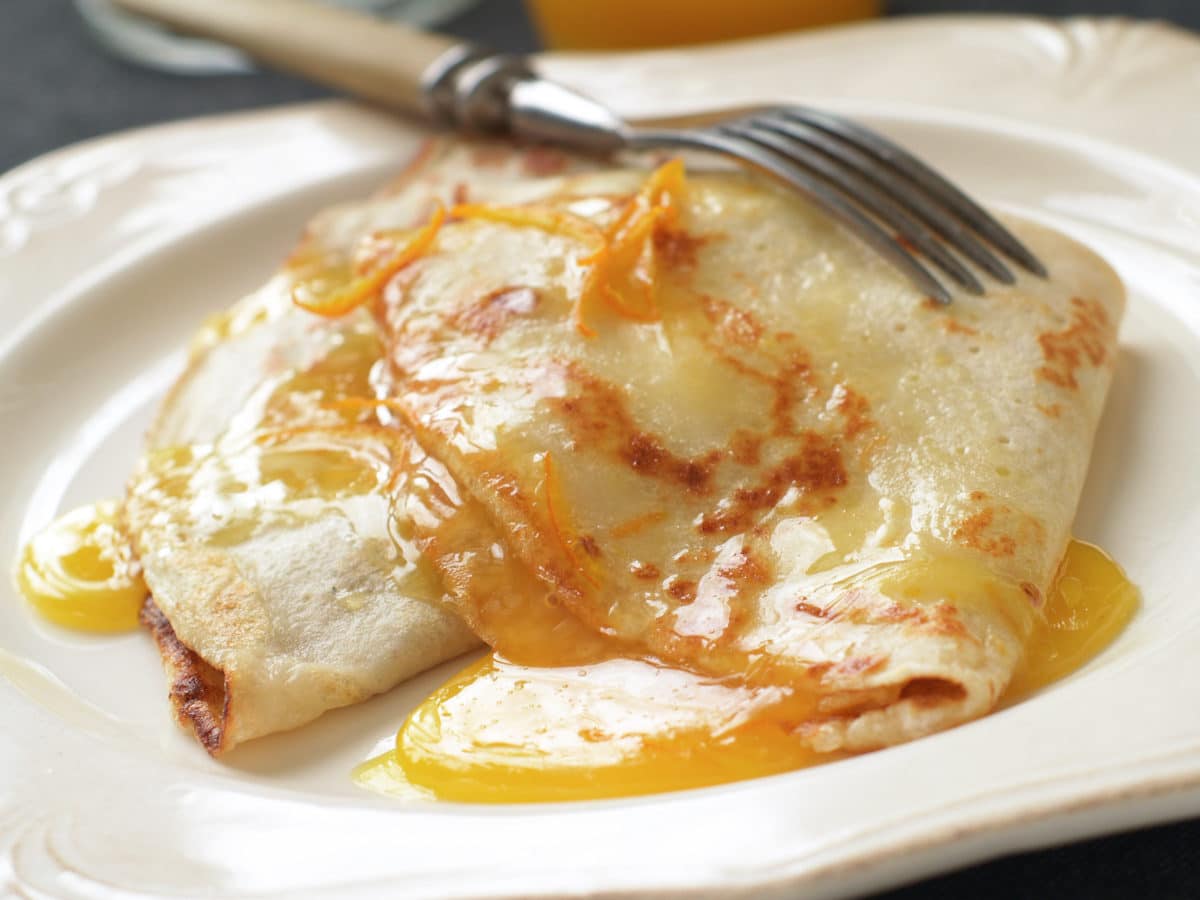 Plate of crêpes drizzled with orange sauce and a fork on the side.