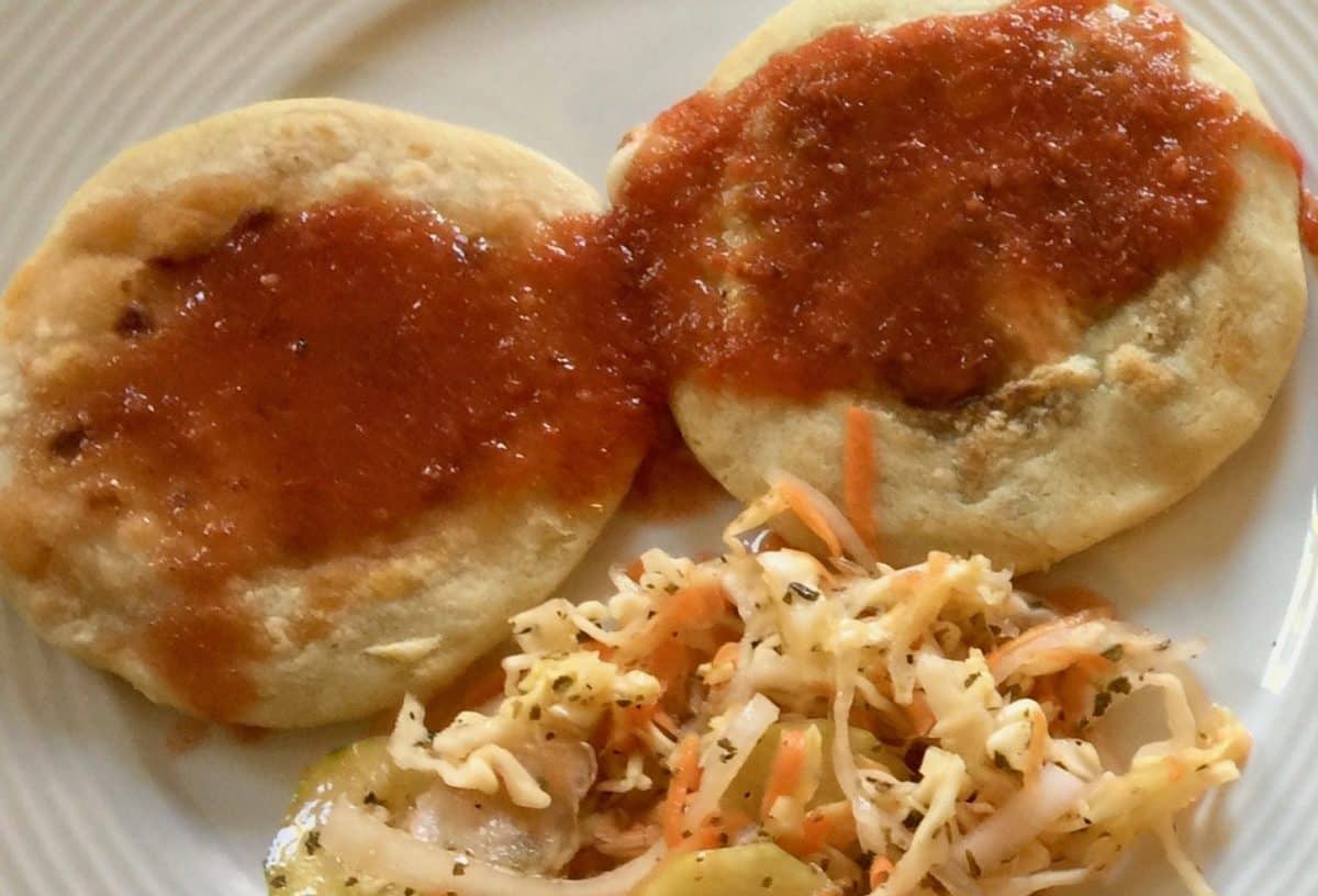 Pupusas topped with tomato sauce, with curtido beside