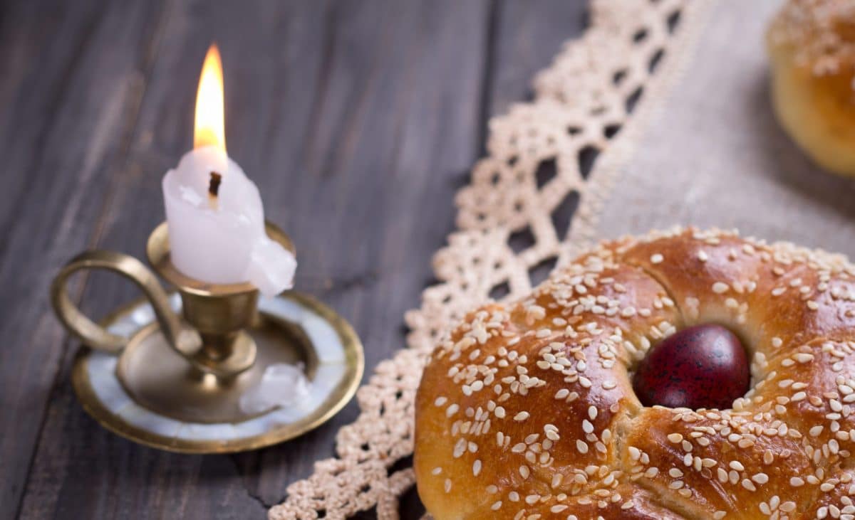 Lit candle with an ornate holder, placed beside a Tsoureki bread