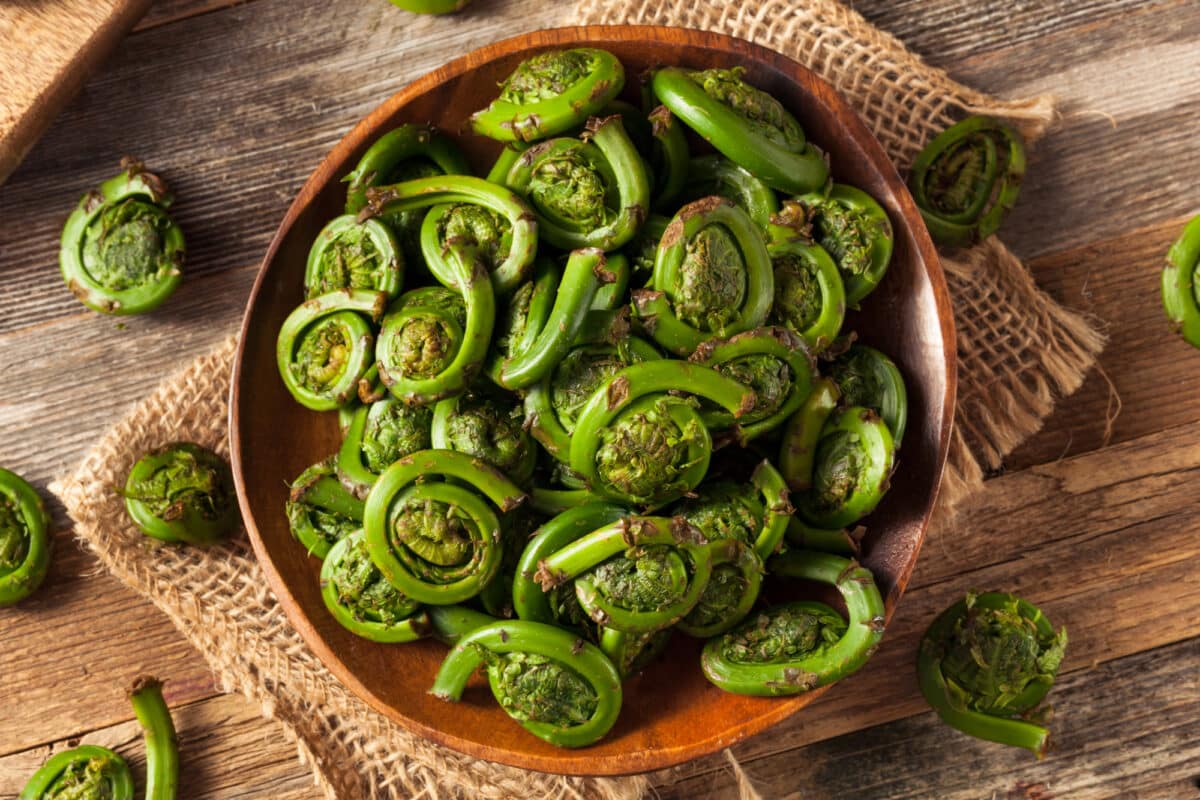 Fiddleheads in a wooden bowl on a piece of burlap, sitting on a wooden tab;le