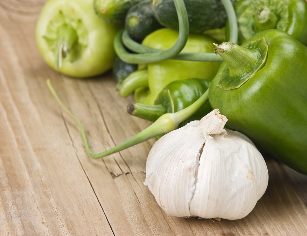 Green bell peppers, sliced cucumber, and a bulb of garlic on a rustic wooden table