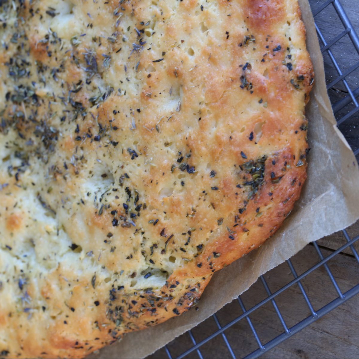Freshly baked focaccia with herbs on a cooling rack.