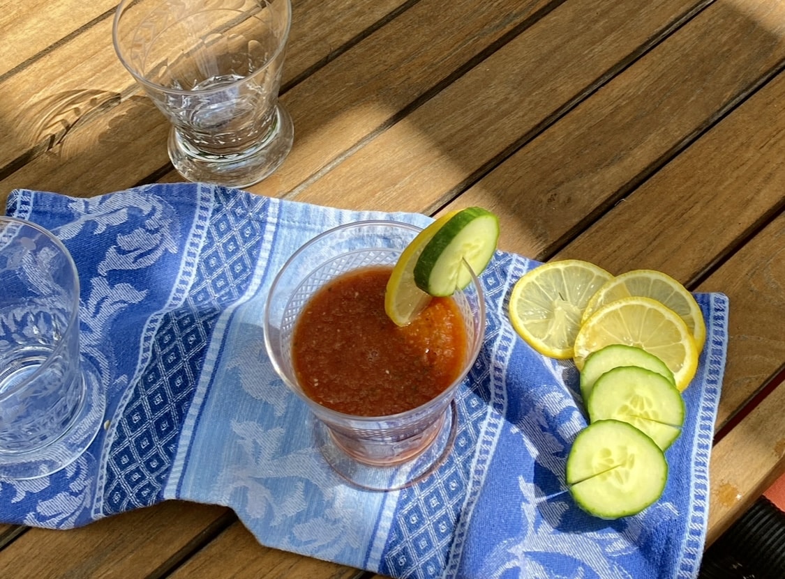A glass of gazpacho garnished with lime on a wooden table.