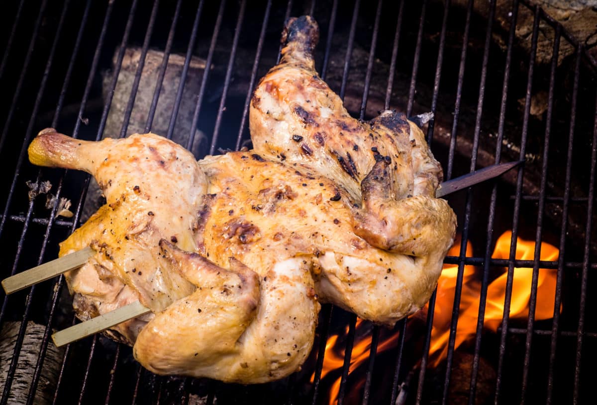 Spatchcocked chicken being grilled over an open flame.
