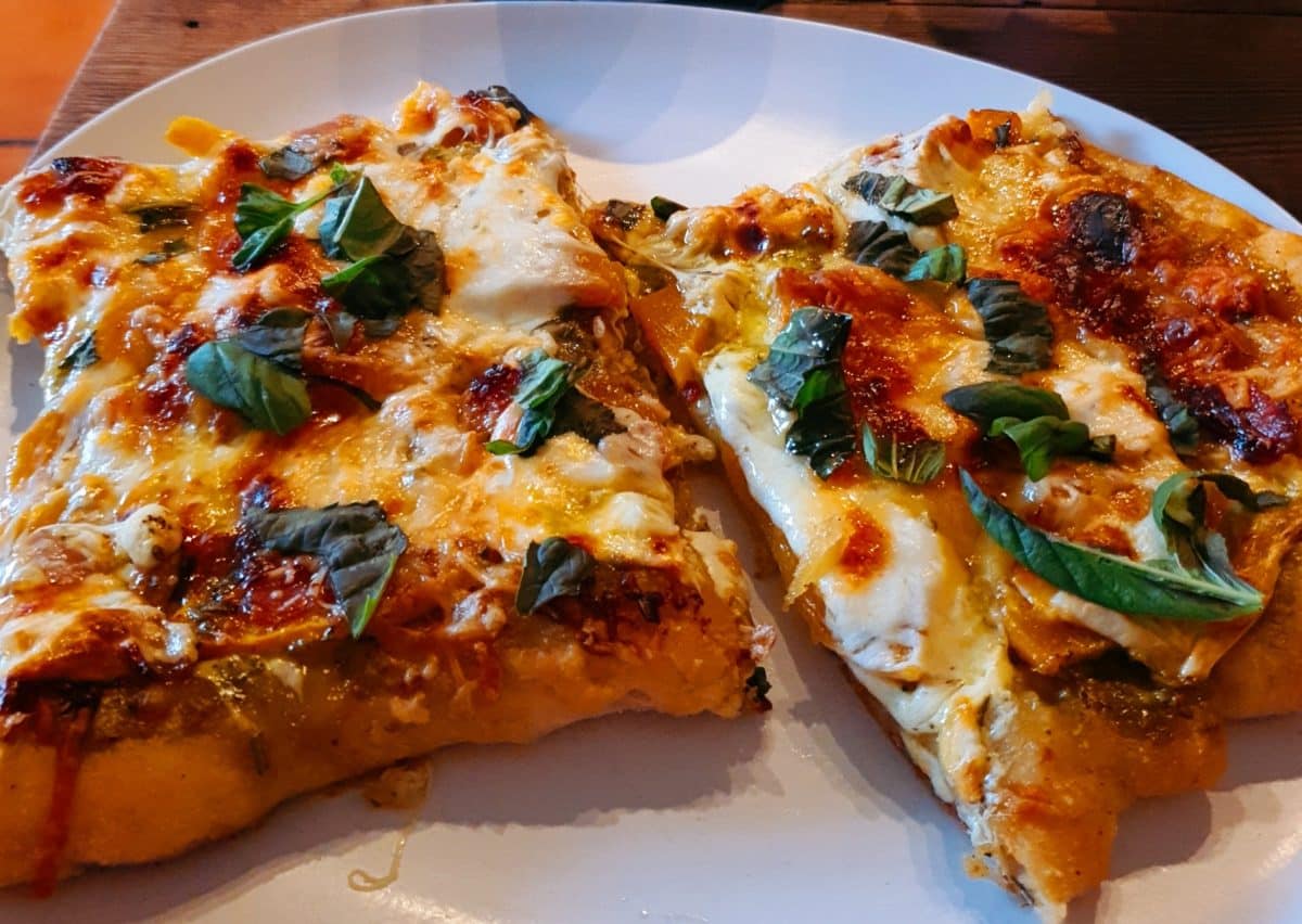 Plate of butternut squash pizza with herbs and cheese.