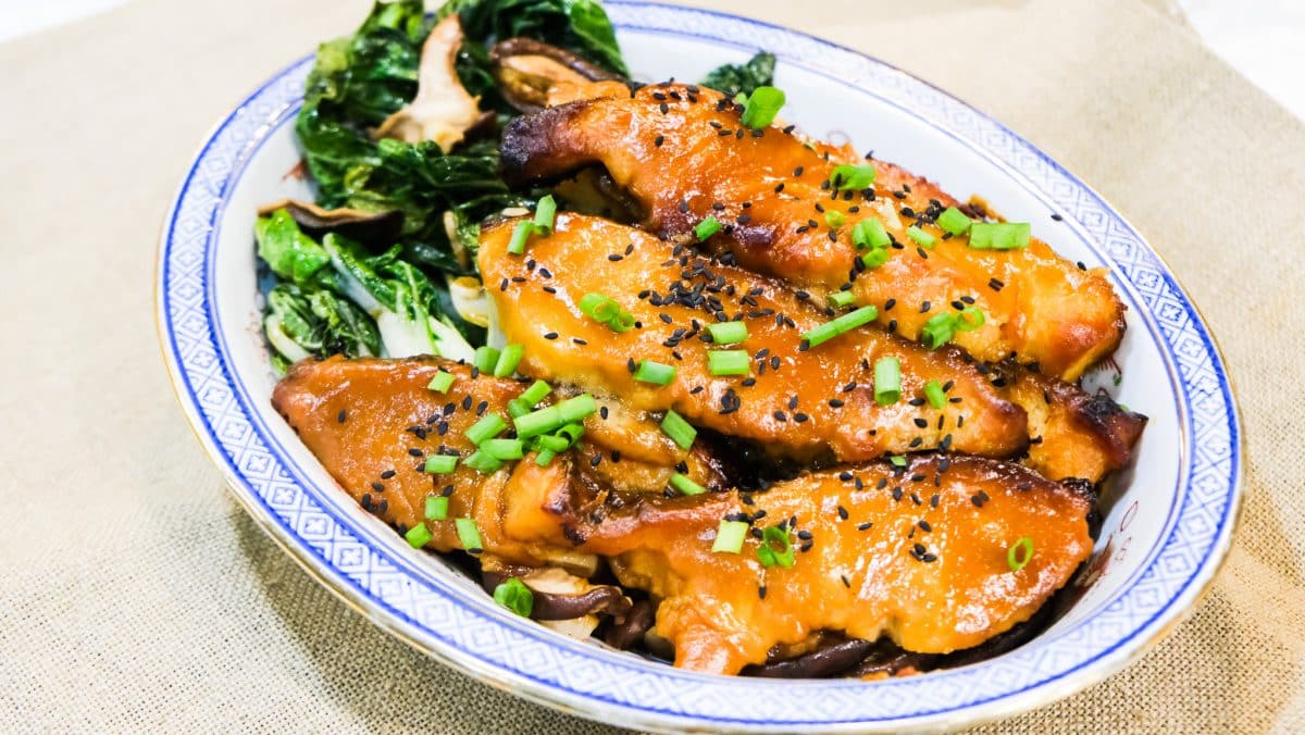 A plated dish of miso marinated cod with bok choy and mushrooms, garnished with green onions and sesame seeds.