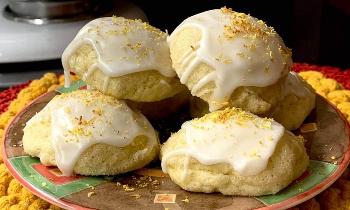 White glazed lemon cookies topped with zest, arranged on a decorative plate.