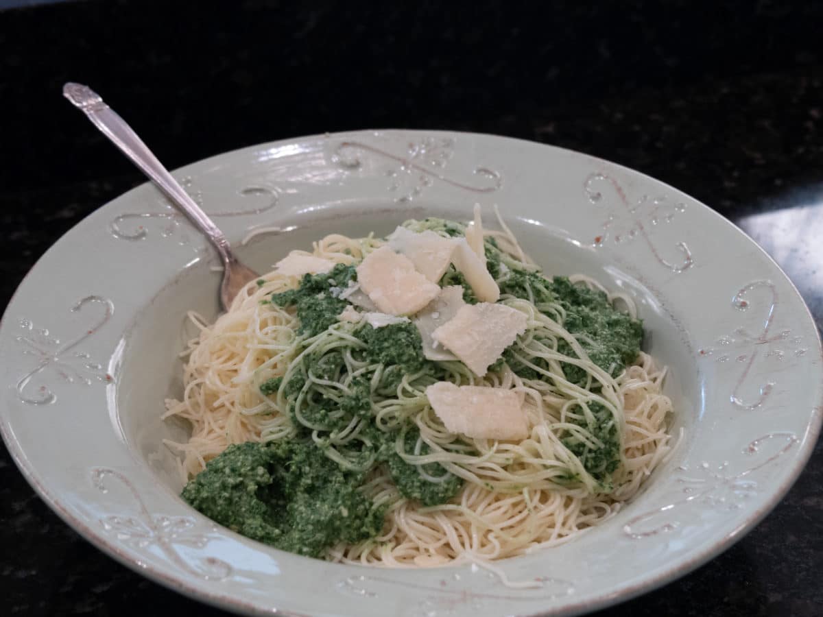 Plate of spaghetti mixed with green nettle pesto, garnished with cheese.