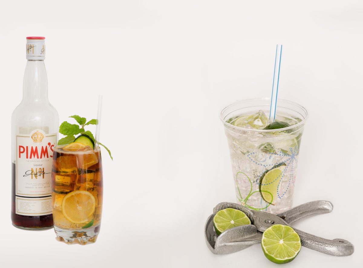 A bottle of Pimm's alongside a refreshing glass of Pimm's and a plastic cup of lime rickey, surrounded by fresh limes.