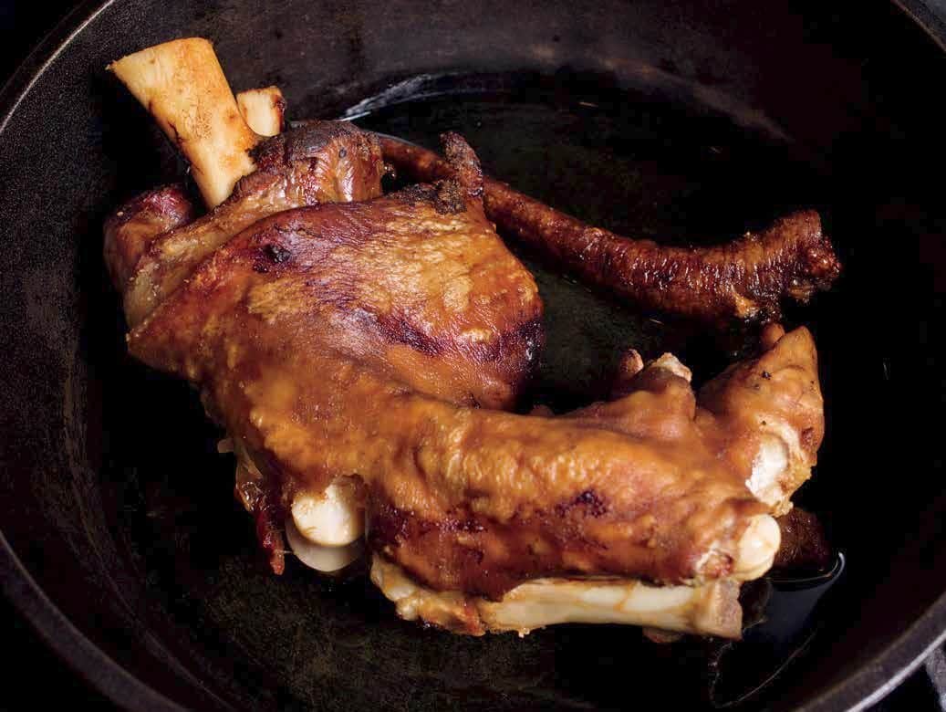 Cooked pork shank confit in a cast-iron pan.