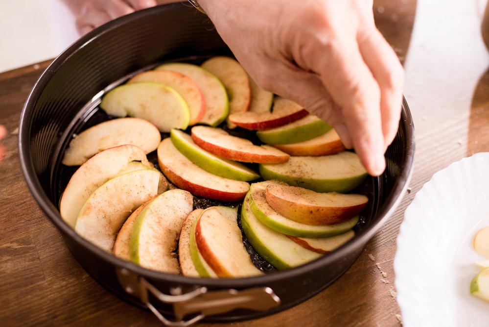 Hands layering apple slices in a pie dish.