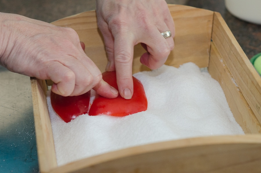 Hands pressing sliced red peppers into a wooden box filled with salt.