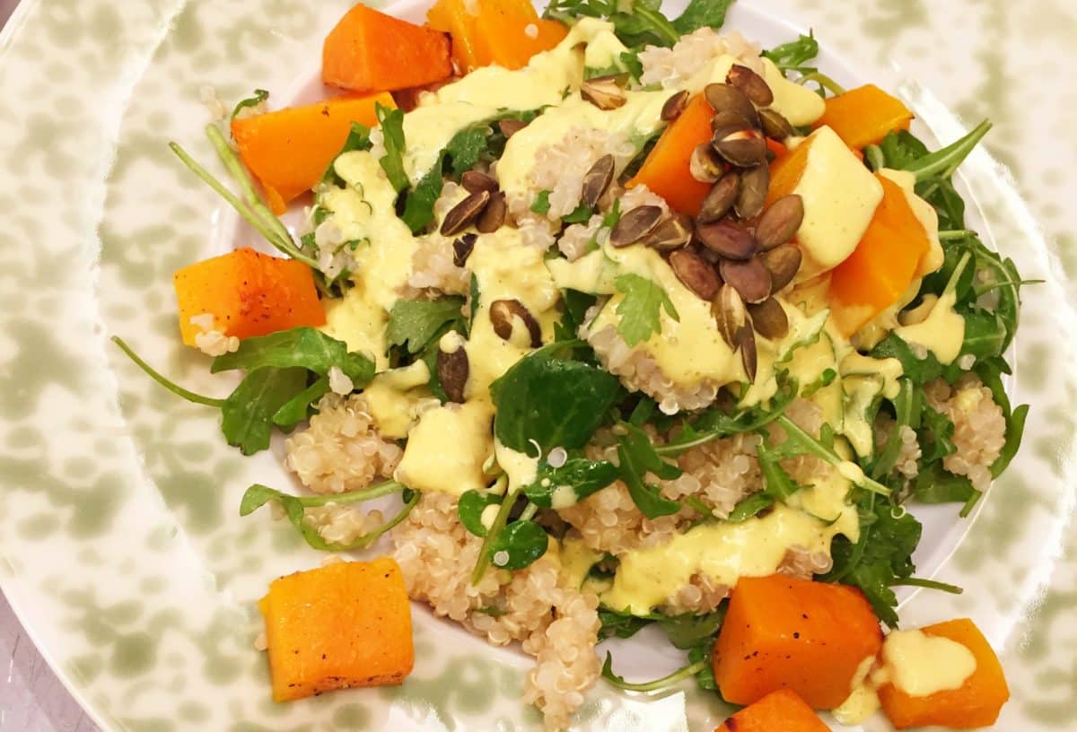 Healthy quinoa salad with chunks of sweet potato, fresh greens, and a drizzle of turmeric tahini hollandaise sauce.