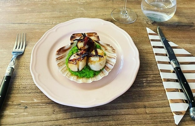 A plated dish of scallops paired with crispy chorizo, set beside a striped napkin.