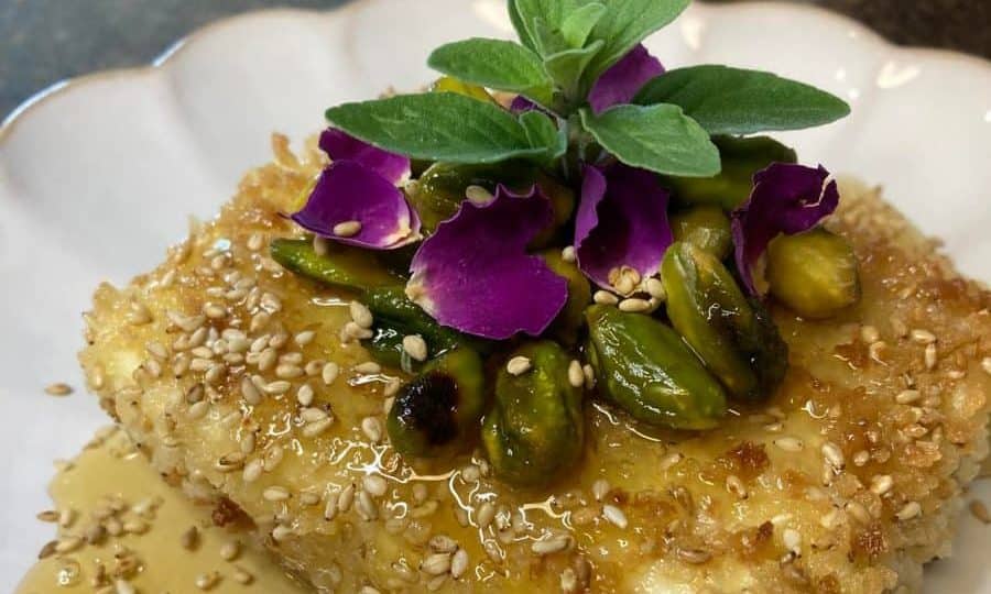 A close-up view of fried feta cheese topped with sesame seeds, fresh herbs, and drizzled honey.