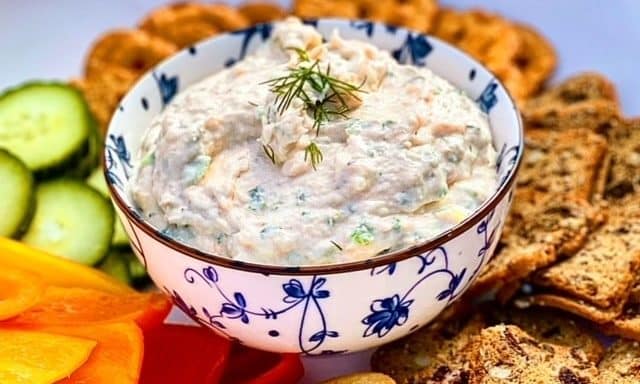 A bowl of smoked salmon dip surrounded by vegetables and crackers