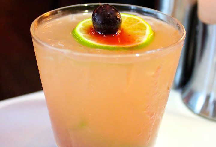 Pink cocktail with lime and berry garnish.