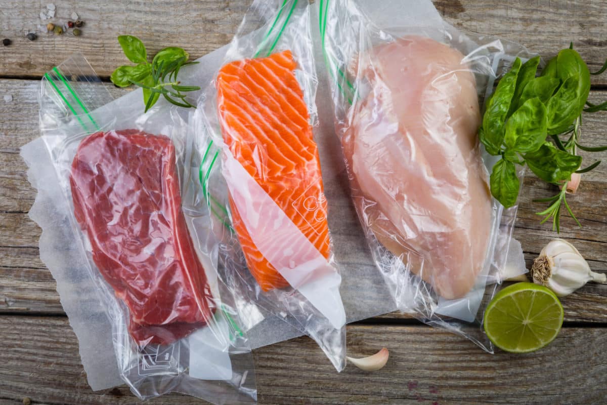 Assorted meats including beef, chicken, and salmon sealed in vacuum plastic bags for sous vide cooking.