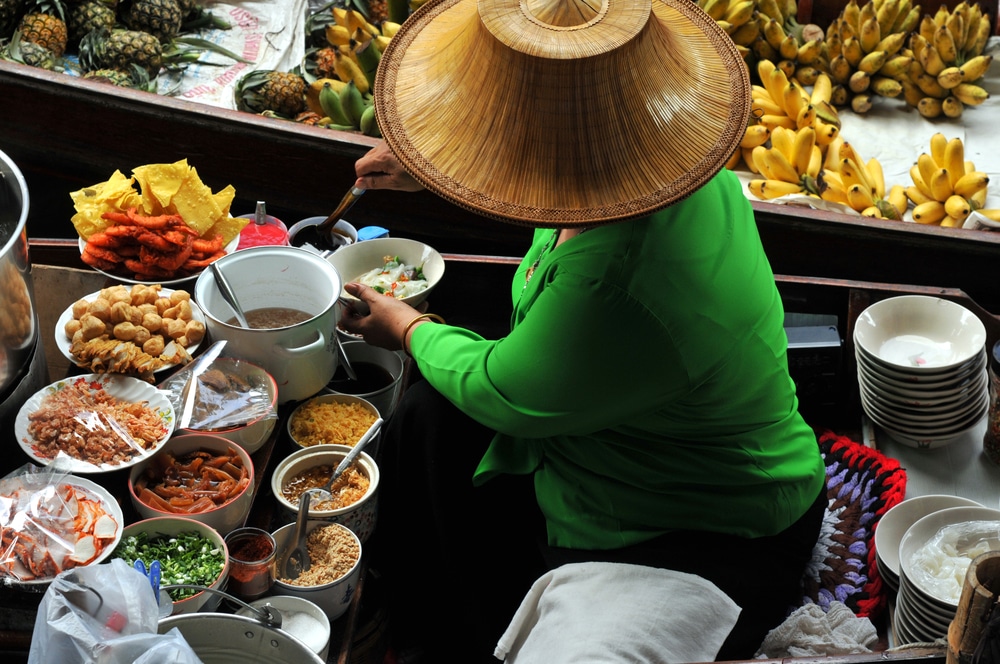 Vendor at a floating market in Thailand selling various dishes and fruits