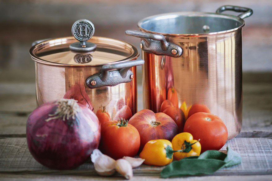 Vintage copper cookware set with fresh vegetables nearby.